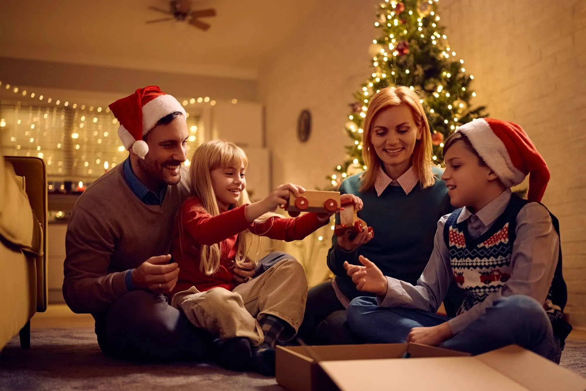 Happy kids having fun while opening Christmas gifts with their parents at home.