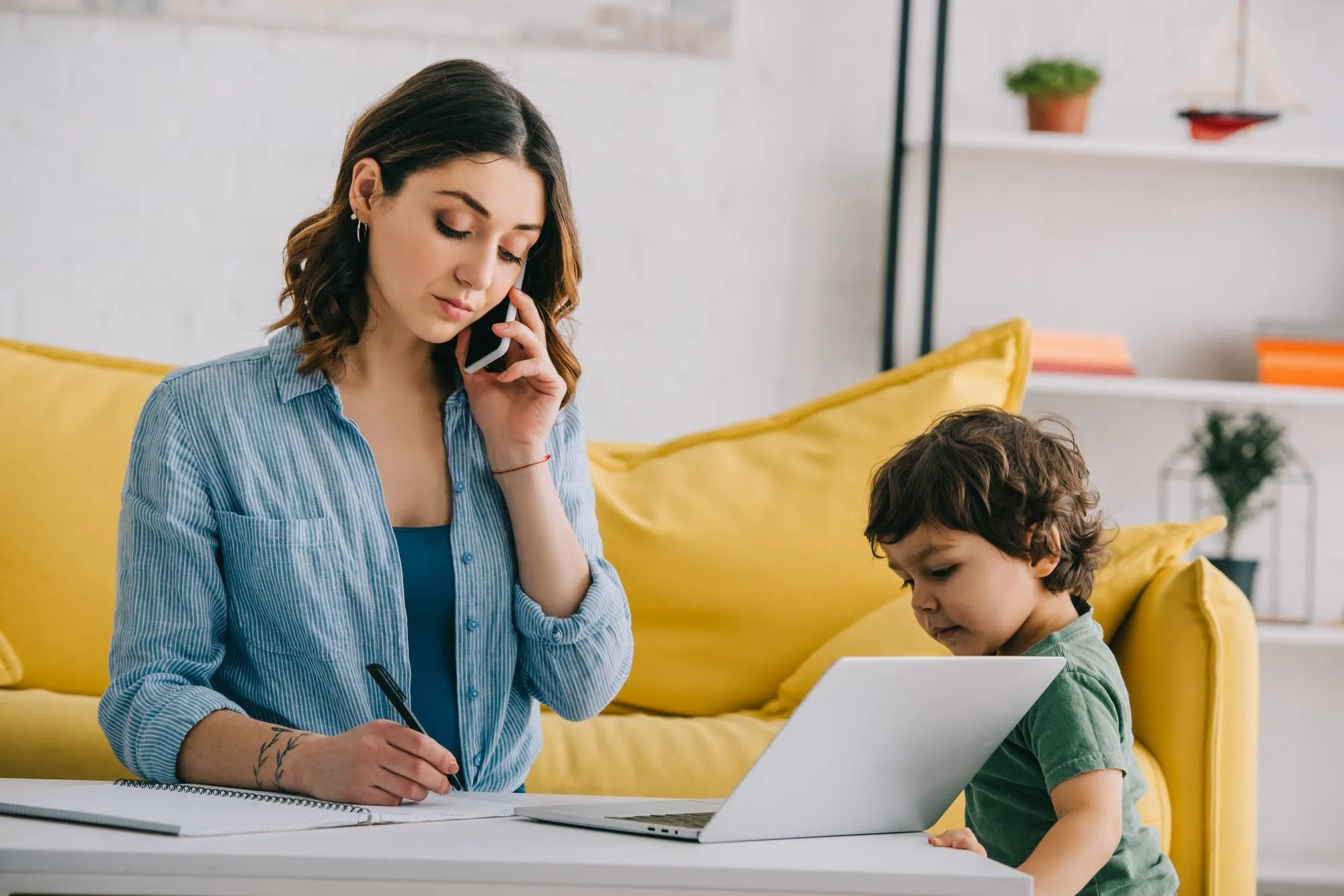 kid looking at laptop while mother talking on smartphone