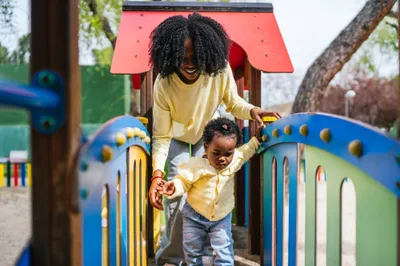 A woman is holding a child's hand as they play on a playground